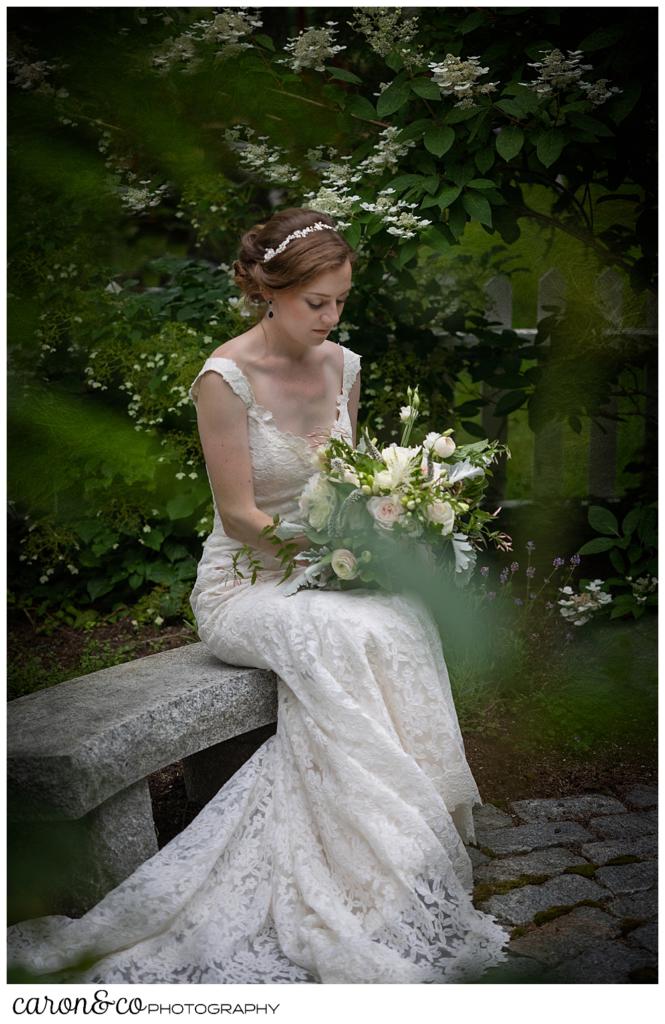 a bride sits on a granite bench in a small garden