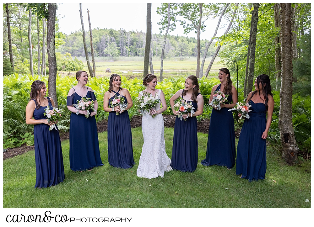 a bride wearing a white dress, and her six bridesmaids wearing blue, stand together in a woodland garden