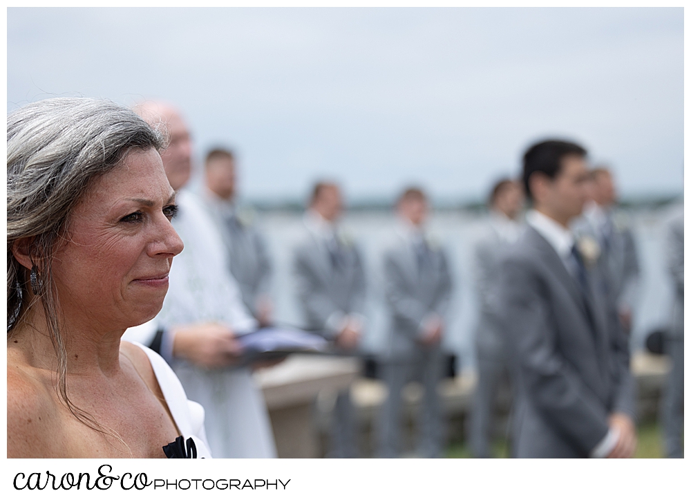 mother of the bride, in the foreground, and groom in the background, watches the bride and her dad walk down the aisle at St. Ann's by-the-sea Episcopal Church, Kennebunkport, Maine