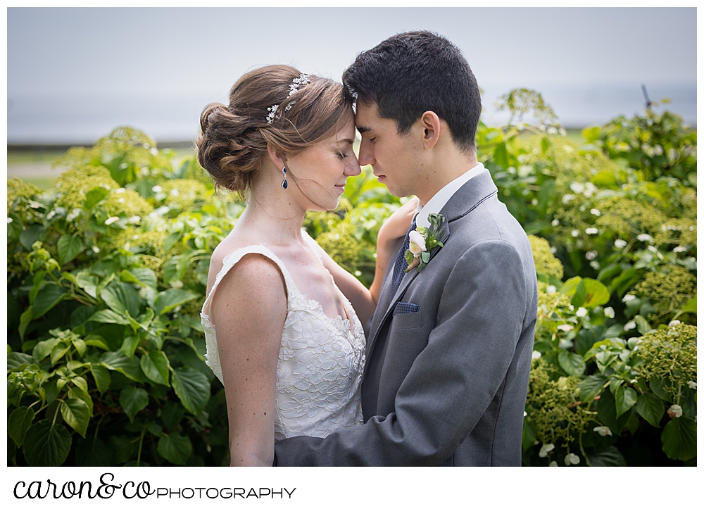 a bride and groom stand in a garden, forehead to forehead