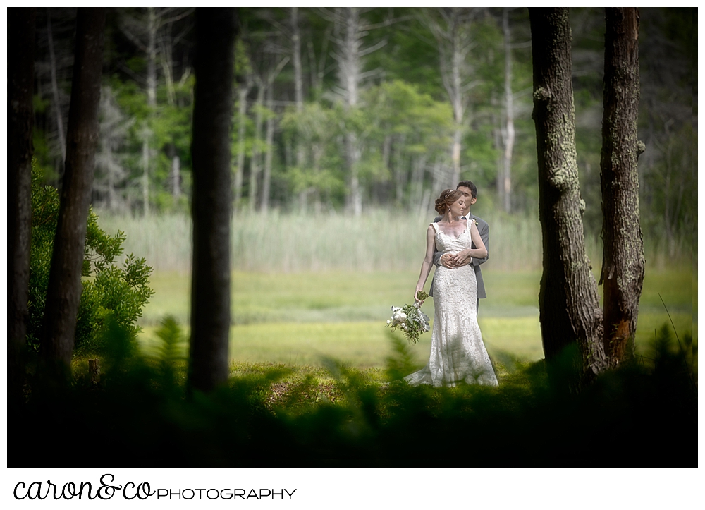 a groom hugs his bride in a a wooded garden, during their Kennebunk Maine wedding reception