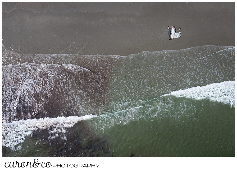 a bride and groom in a Gooch's Beach drone photo with them couple lying on the sand, and the water at their feet