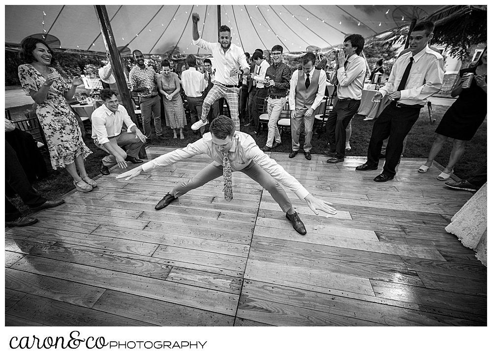 black and white photo of a man dancing, his arms and legs spread wide, during a tented Kennebunk Maine wedding reception