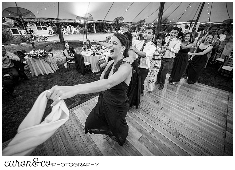 black and white photo of a woman holding onto a scarf, she is leading a conga line dance during a tented Kennebunk Maine wedding reception