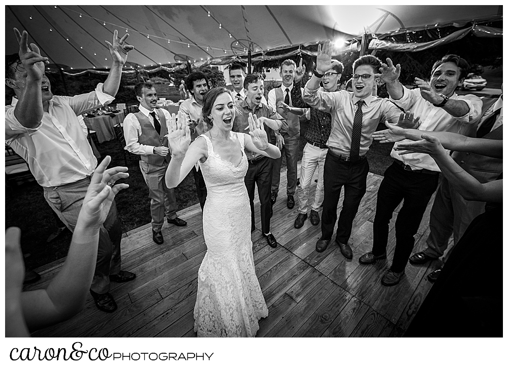 black and white photo of a bride standing on the dance floor, surrounded by guests who are singing during a Maine coast tented wedding