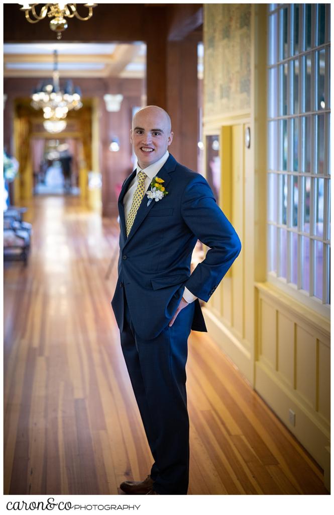 full length portrait of a groom, wearing a medium blue suite, standing in the hallway of the colony hotel, Kennebunkport maine