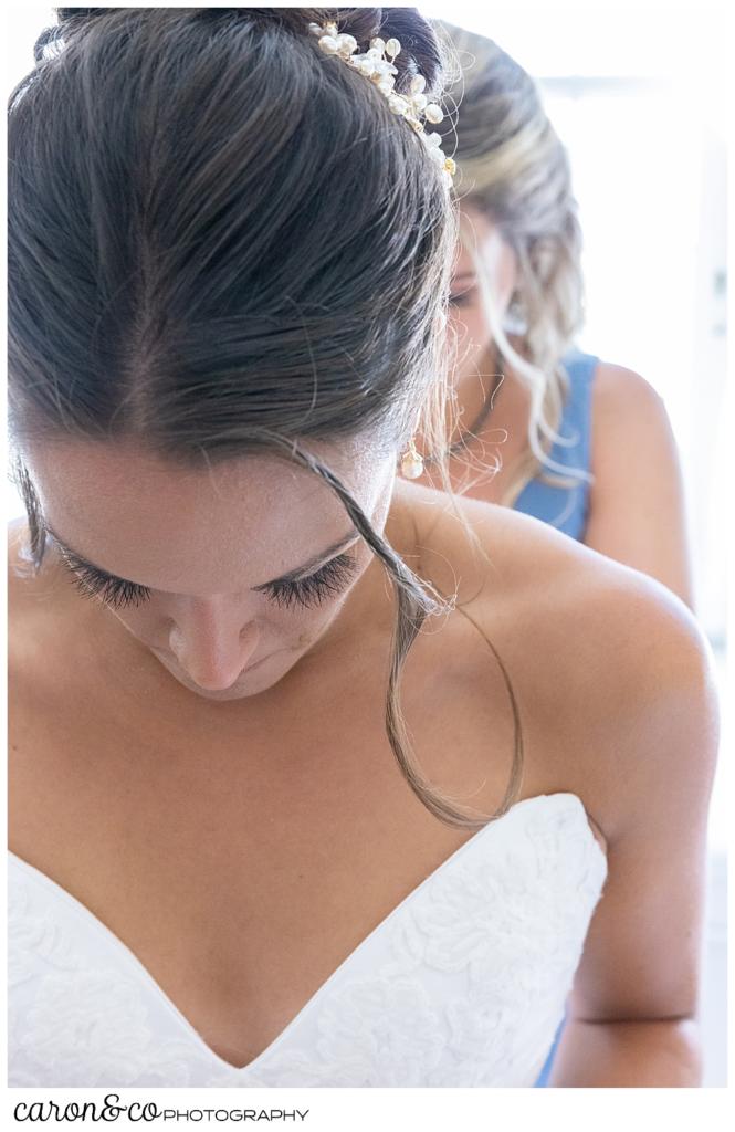 a bride having her dress zipped, has her head down, as a bridesmaid zips in the background