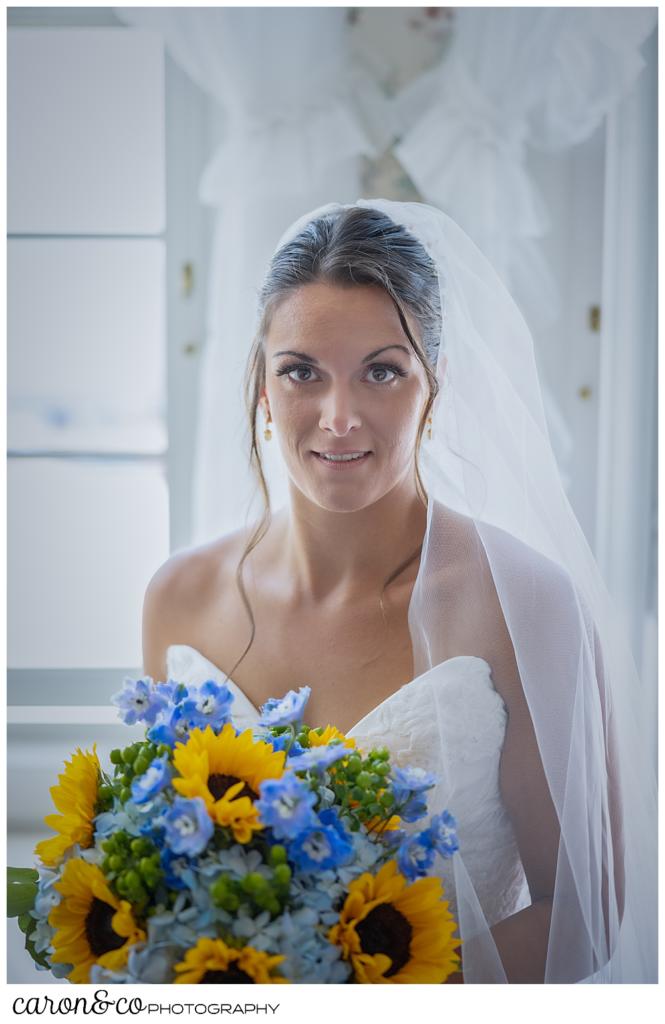 a beautiful bridal portrait of a dark haired, dark eyed bride, wearing a white sleeveless dress and veil, holding a bouquet of blue hydrangeas and yellow sun flowers, she has a slight smile