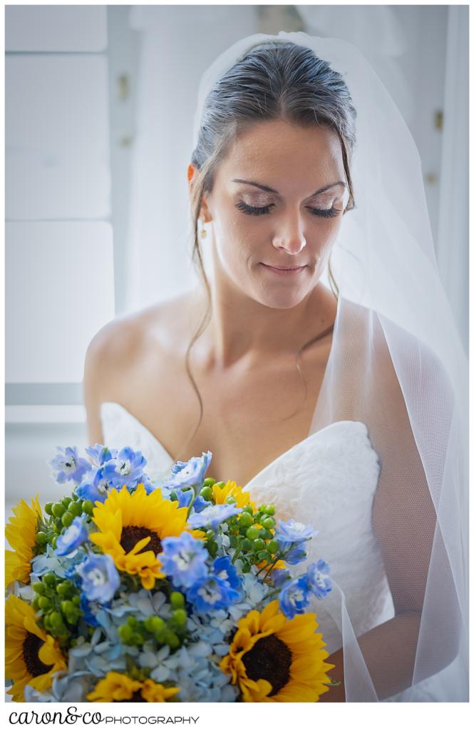 a stunning bridal portrait of a dark haired bride, her head to the right, eyes closed, wearing a white strapless gown and veil, holding a bridal bouquet of blue hydrangeas and yellow sun flowers