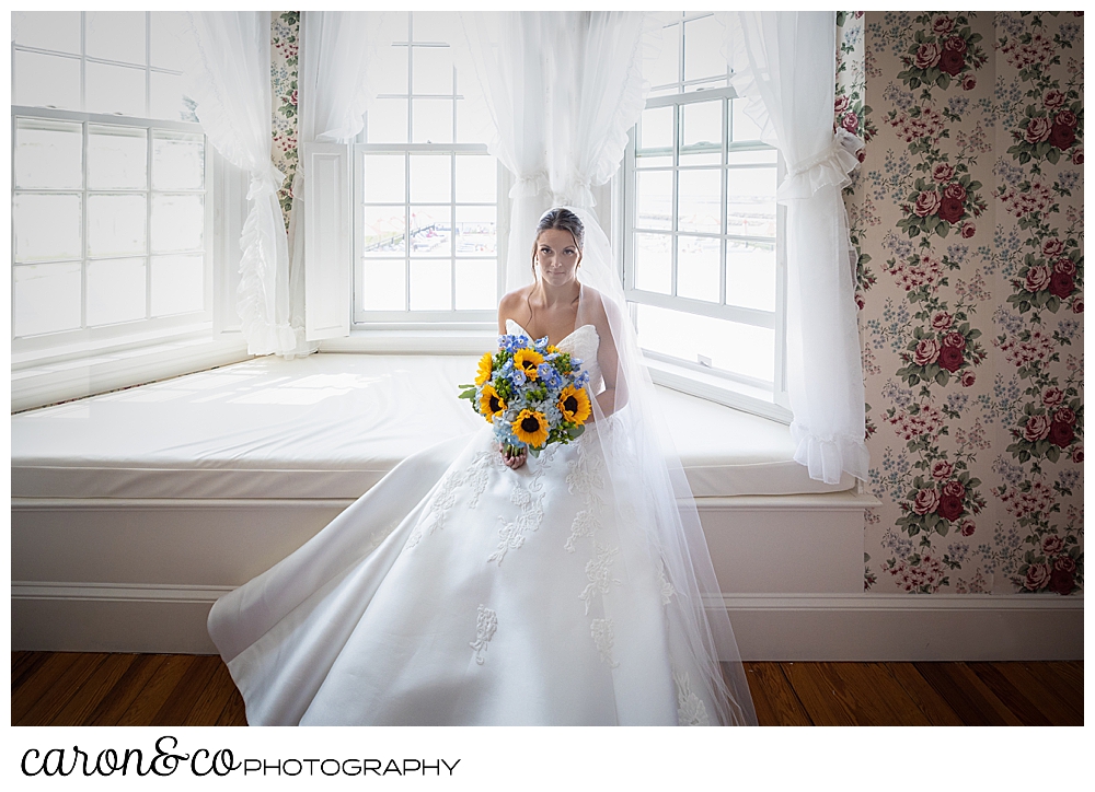 a gorgeous bride with dark hair and eyes, sits on the window seat at the Colony Hotel, she's holding a bouquet of blue hydrangeas and yellow sun flowers,