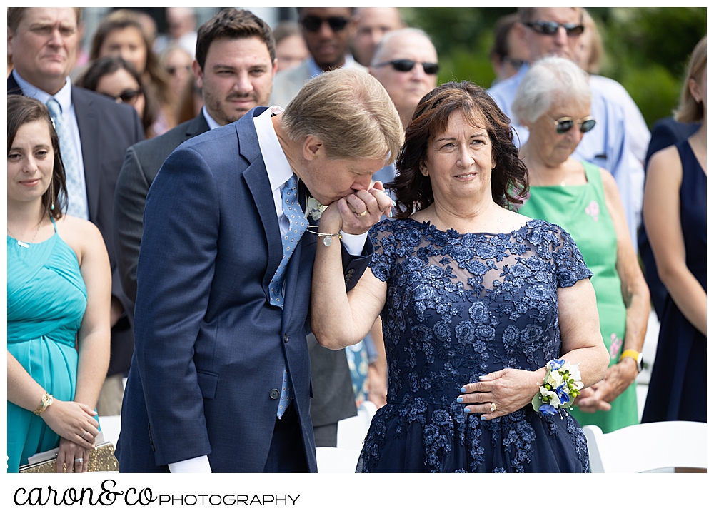 a man in a blue suite, kisses the hand of a woman wearing a blue lace dress