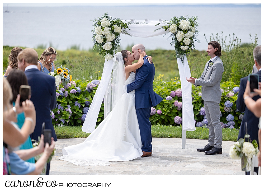 a bride and groom share their first kiss in front of an arbor at a Kennebunkport wedding at the Colony Hotel