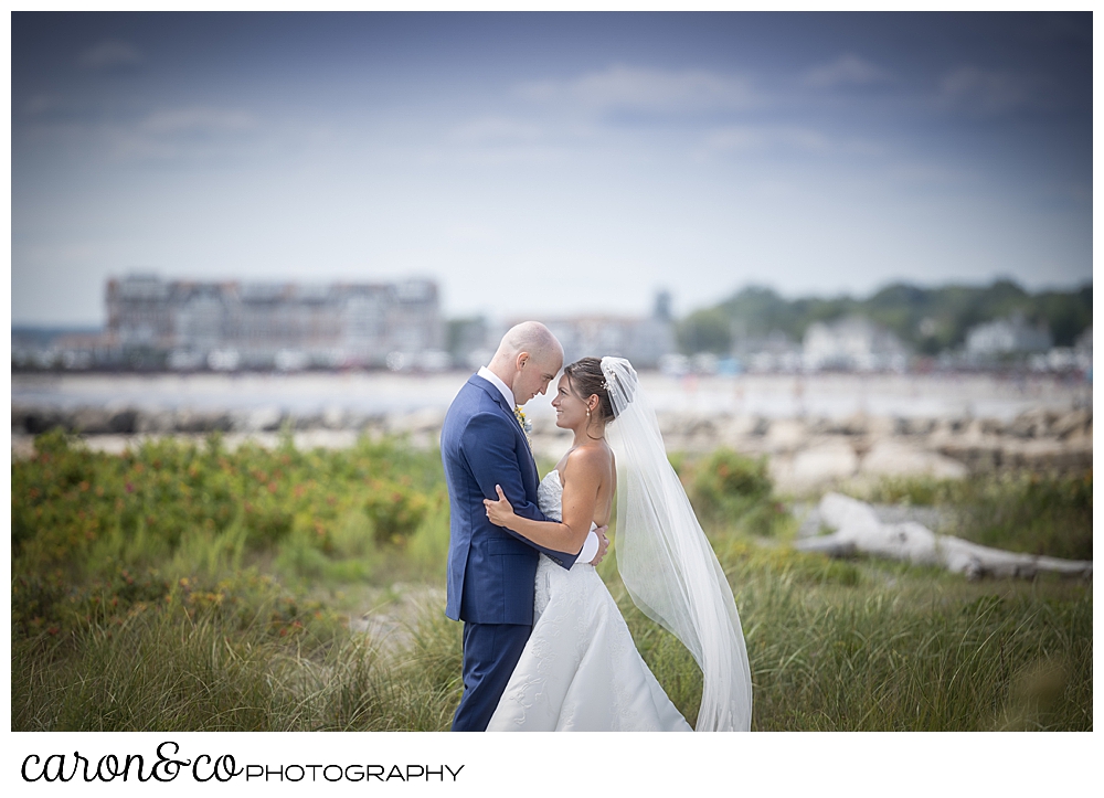 a bride and groom stand facing each other, fore heads together, in the dunes at Colony Beach, at a Kennebunkport wedding at the Colony Hotel