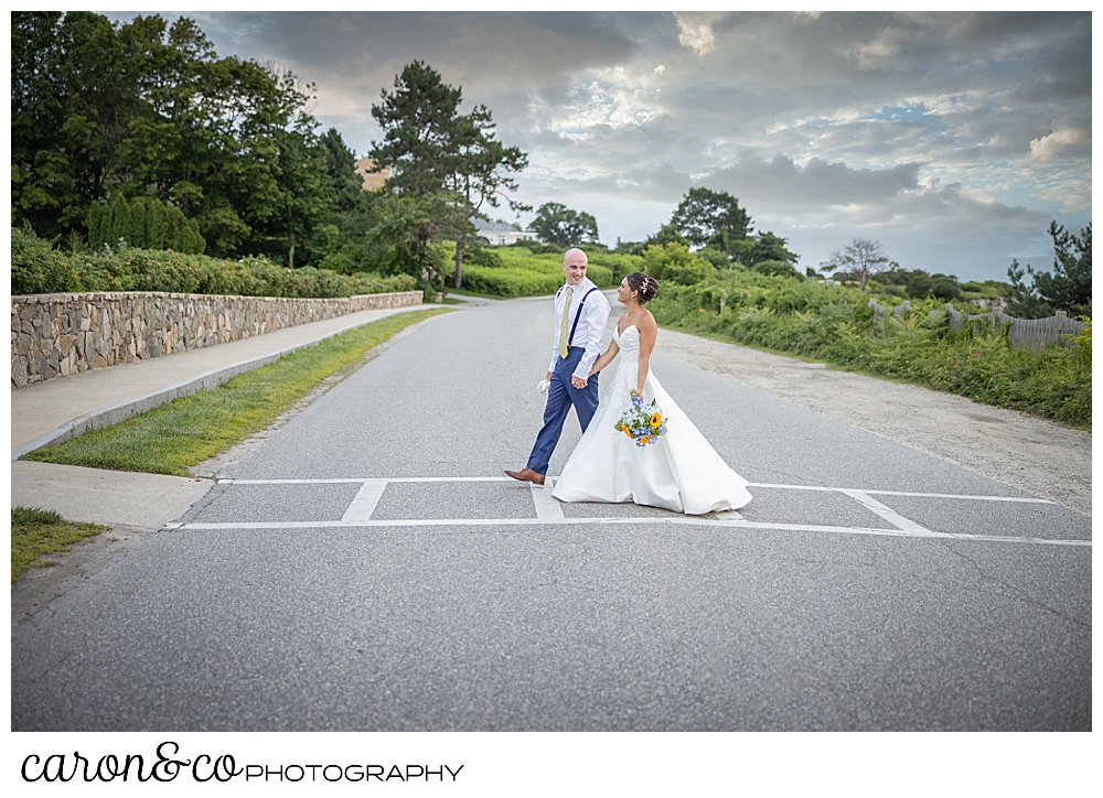 a bride and groom holding hands, cross the street in front of the Colony Hotel, at a Kennebunkport wedding at the Colony Hotel