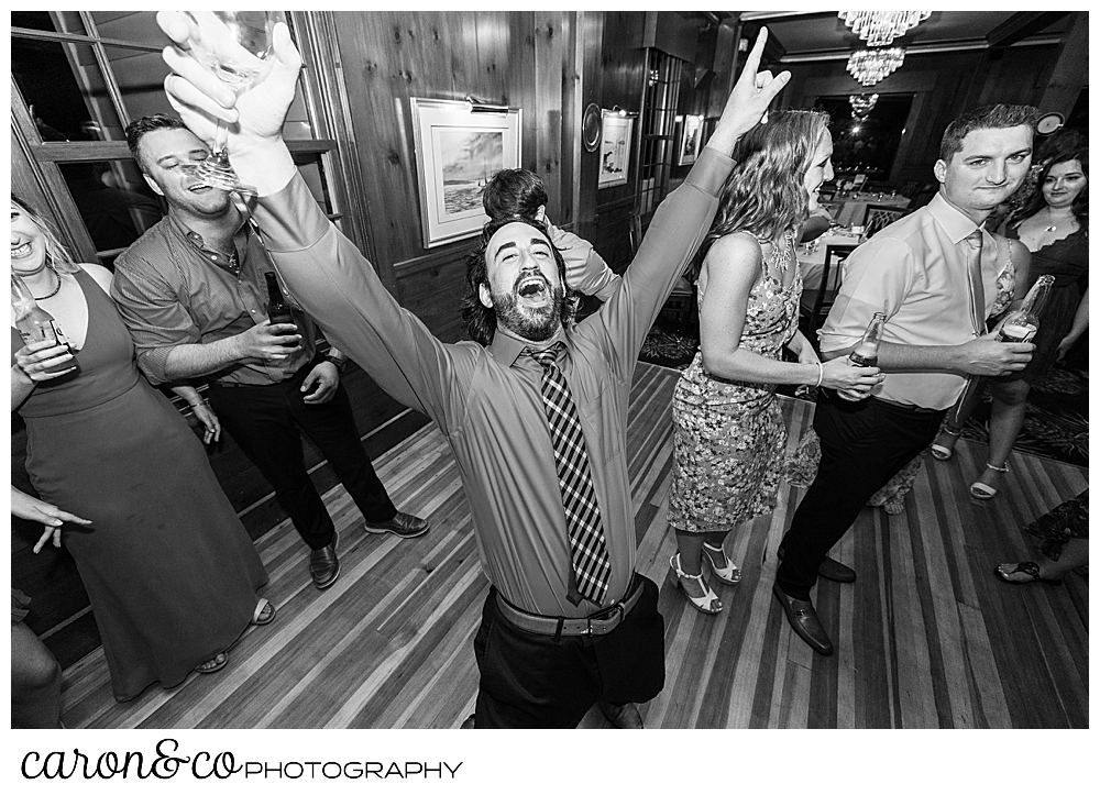 black and white photo of a man with his arms raised and his mouth open, while guests dance in the background