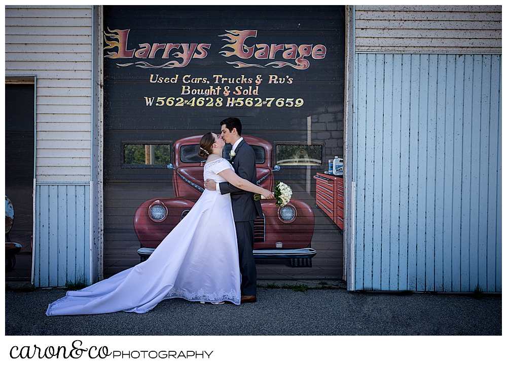 a bride and groom kiss in front of a car mural in Peru Maine, during a sweet western Maine wedding