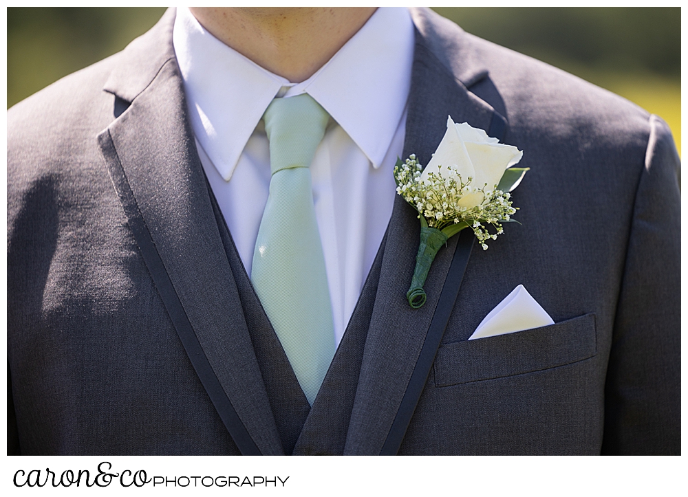 groom details of a green tie, a cream rose boutonniere, and a white pocket square,