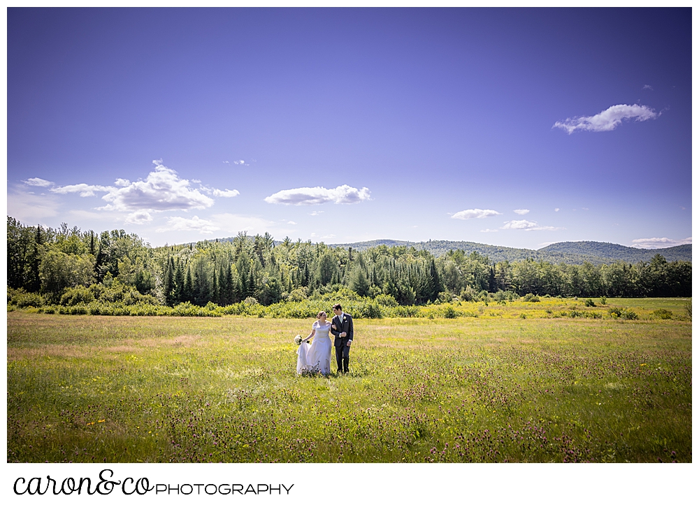 a bride and groom walking in a field, arms linked, during a sweet western Maine wedding