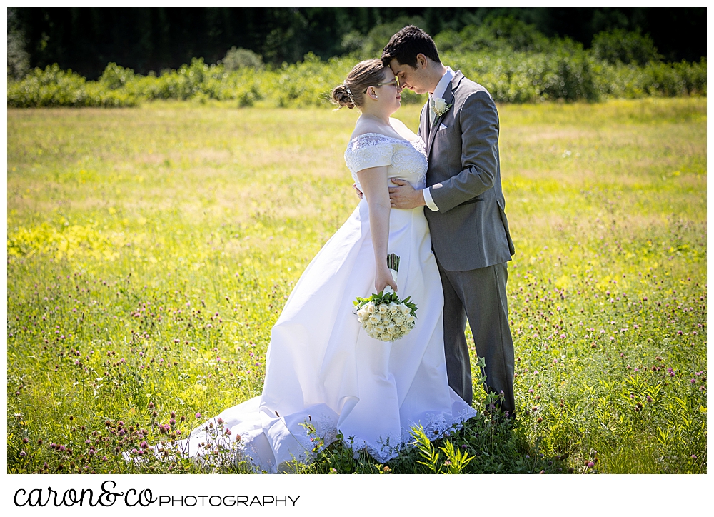 a bride and groom standing with their foreheads touching, in a field