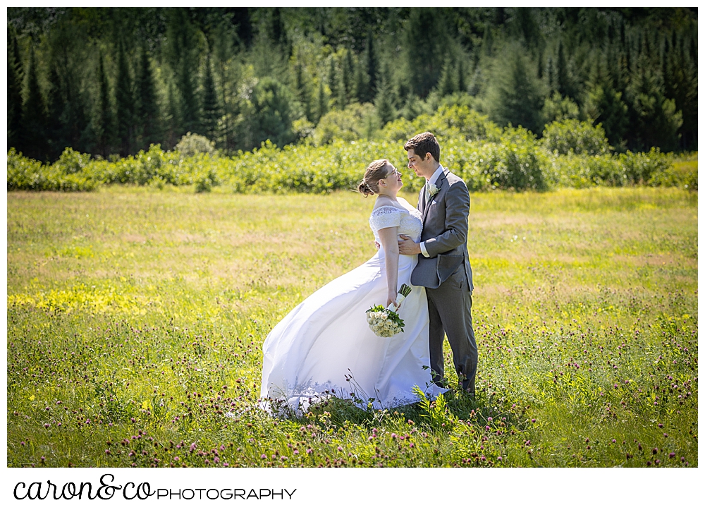 a bride and groom stand in a field, facing each other, their arms around each other