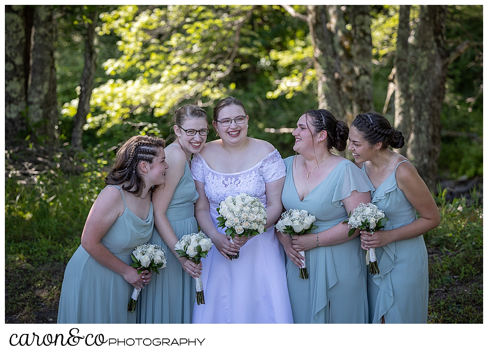 a bride in white, and her bridesmaids in sage green, huddled together, laughing