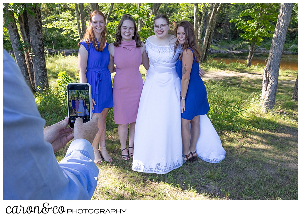 a bride and her friends standing together, while they get their photo taken with a friends phone