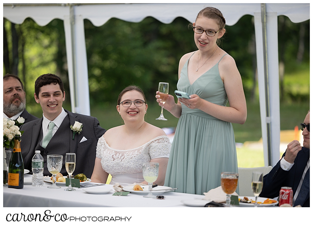 a bridesmaid holds a glass of champagne and her phone during a toast at a sweet western Maine wedding reception