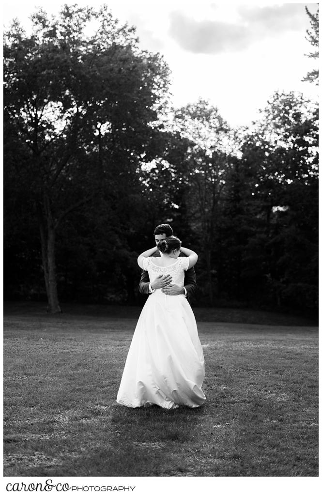 black and white photo of a bride and groom dancing in a field, the bride's back is to the camera