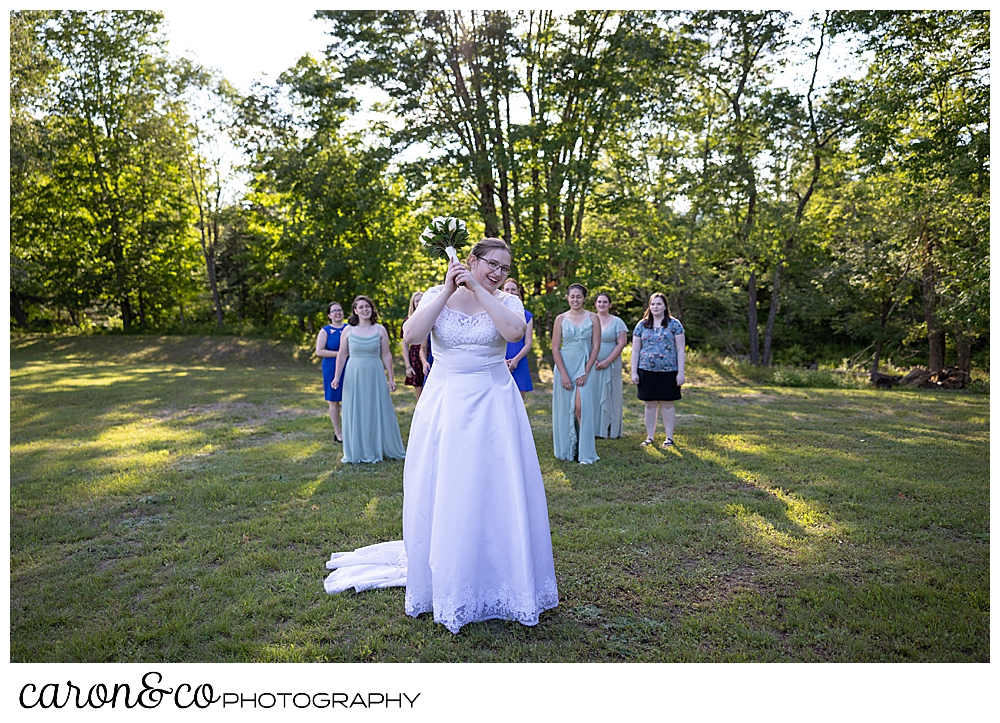 a bride stands ready to toss her bouquet, while the single ladies gather behind her