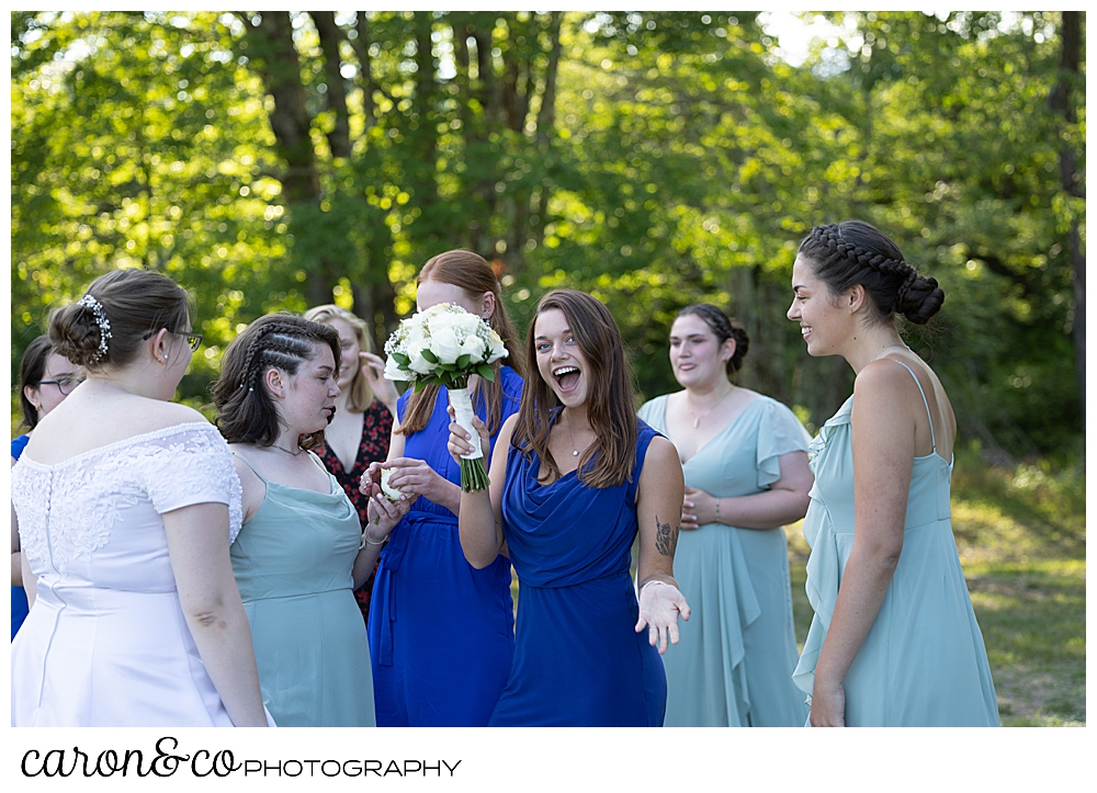 a bride and a group of women gather around a woman who caught the bouquet, she is looking at the camera