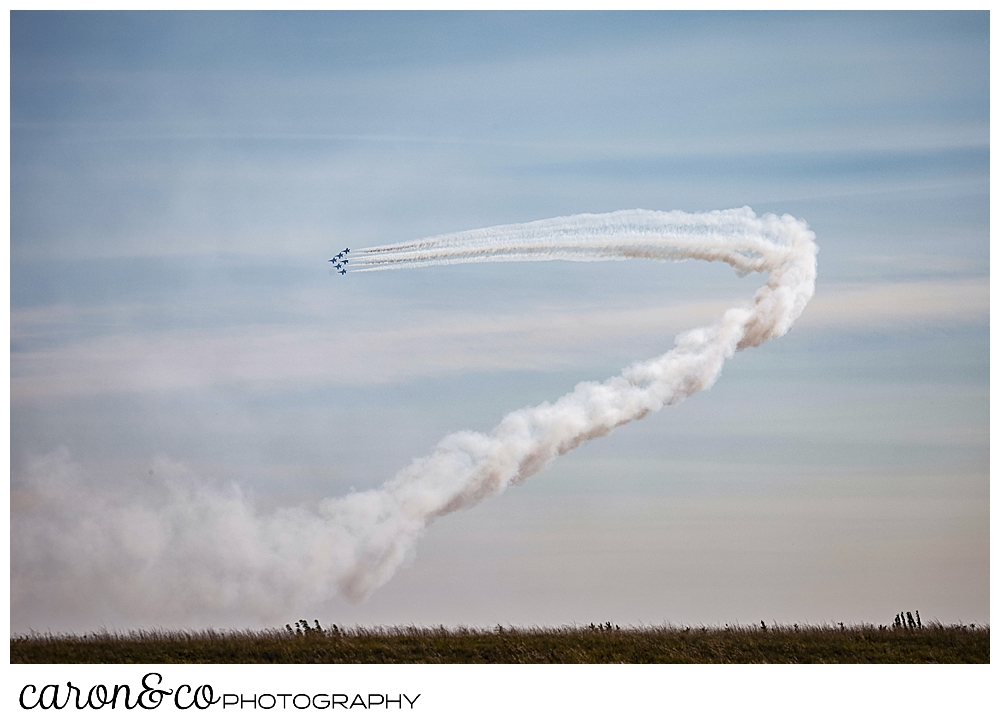 5 blue angels from the us navy fly in a diamond in the far distance, their contrails flaring out behind them