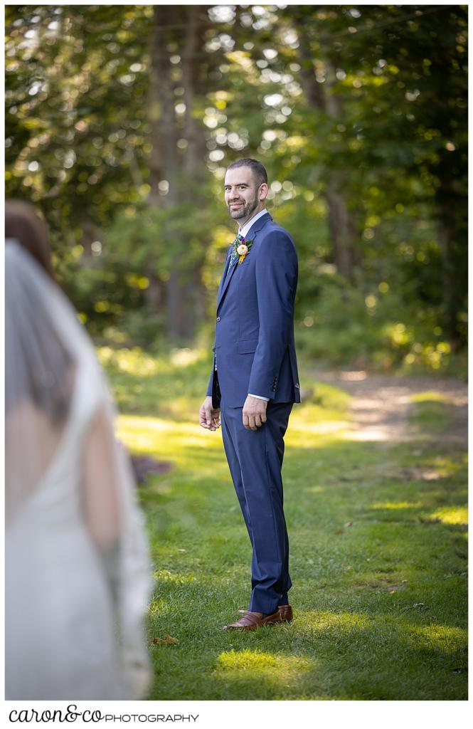 a groom, in the background, wearing a blue suit, turns to see his bride in the foreground, during their camp skylemar wedding day first look