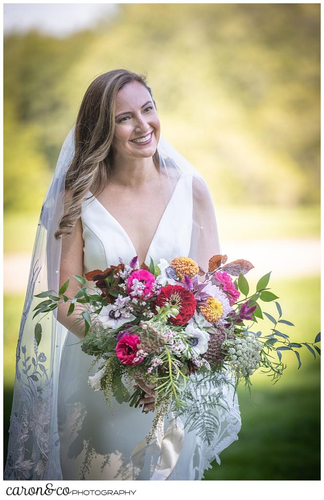 a bride wearing a sleeveless white dress and veil, carrying a bride bouquet of flowers, smiles as her groom approaches during their Camp Skylemar wedding day first look