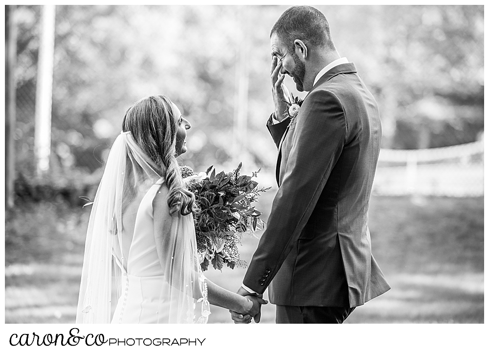 a black and white photo of a bride and groom facing each other, holding hands, the groom as his hand to his eyes, during their Camp Skylemar wedding day first look