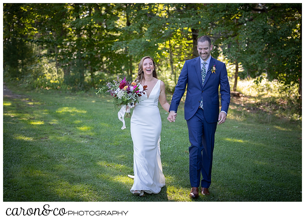 a smiling bride and groom walk hand in hand in a grassy field