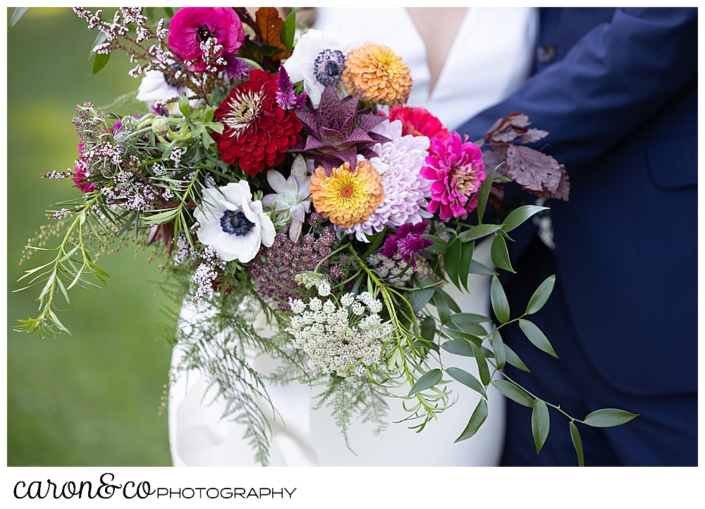 a bridal bouquet of bright flowers by Bounty O Blooms, is held by the bride as the groom hugs her