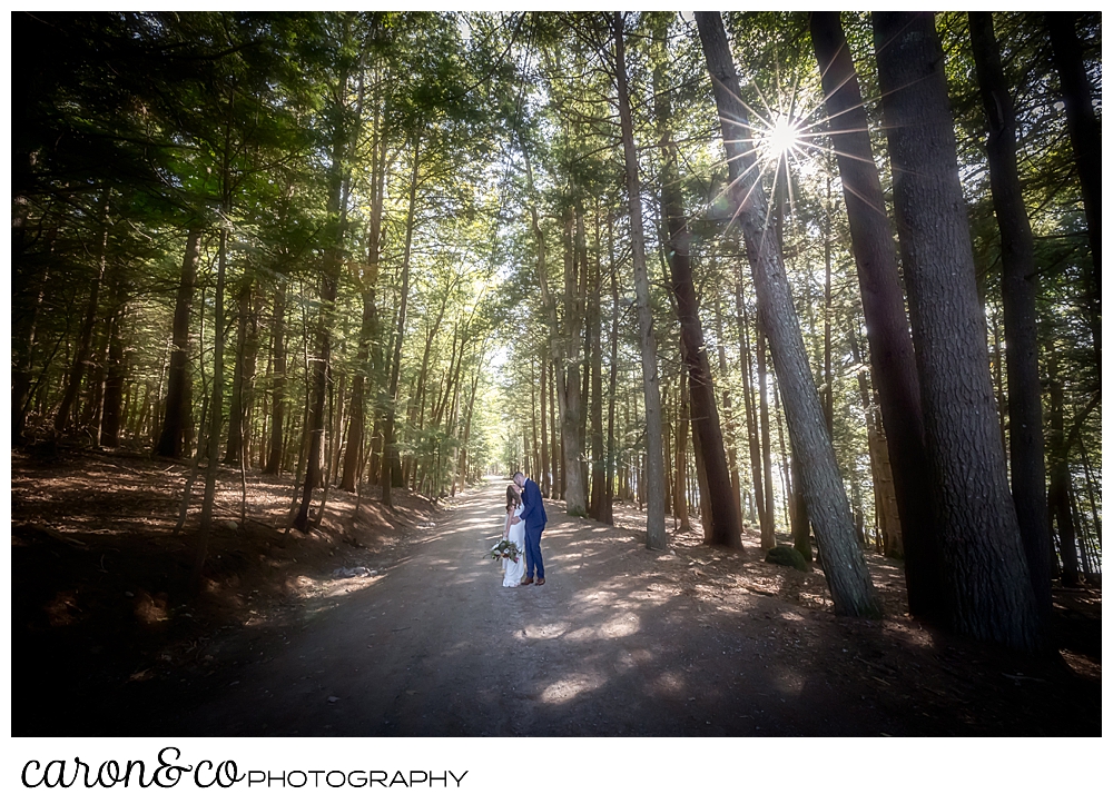 a bride and groom kiss while walking on a dirt road with tall trees all around