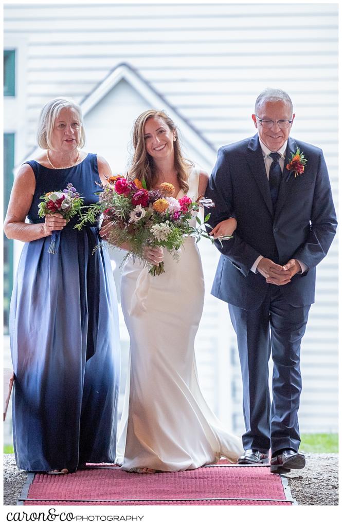 a bride walks down the aisle with her mother and father on either side