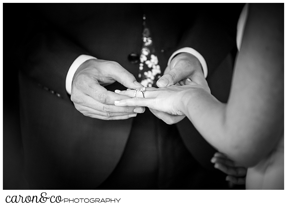 a black and white photo of a groom putting a wedding band on his bride