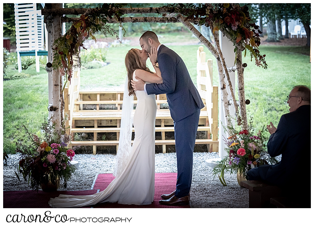 a bride and groom have their first kiss under a birch branch arbor at a camp skylemar wedding ceremony