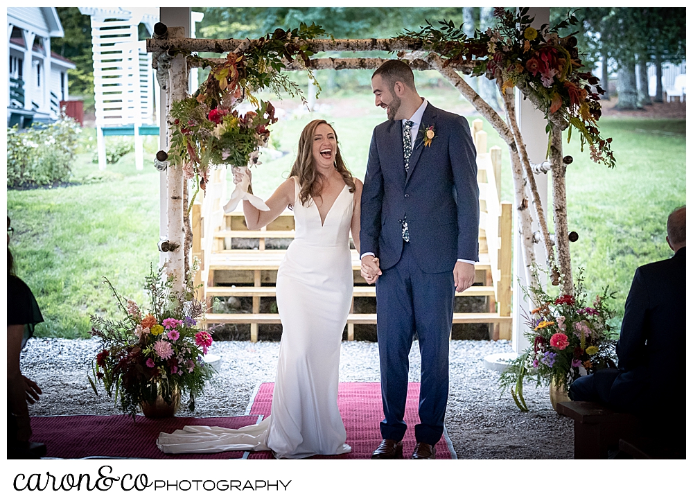 a smiling bride holds the hand of her smiling groom, and her bouquet is held aloft