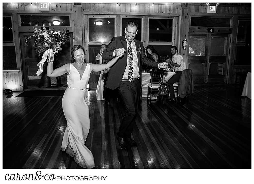 black and white photo of a bride and groom entering their camp skylemar wedding reception, they're both laughing