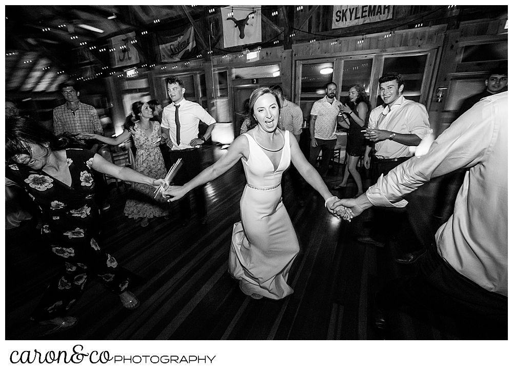 black and white photo of a bride holding hands with her wedding guests, and dancing and singing