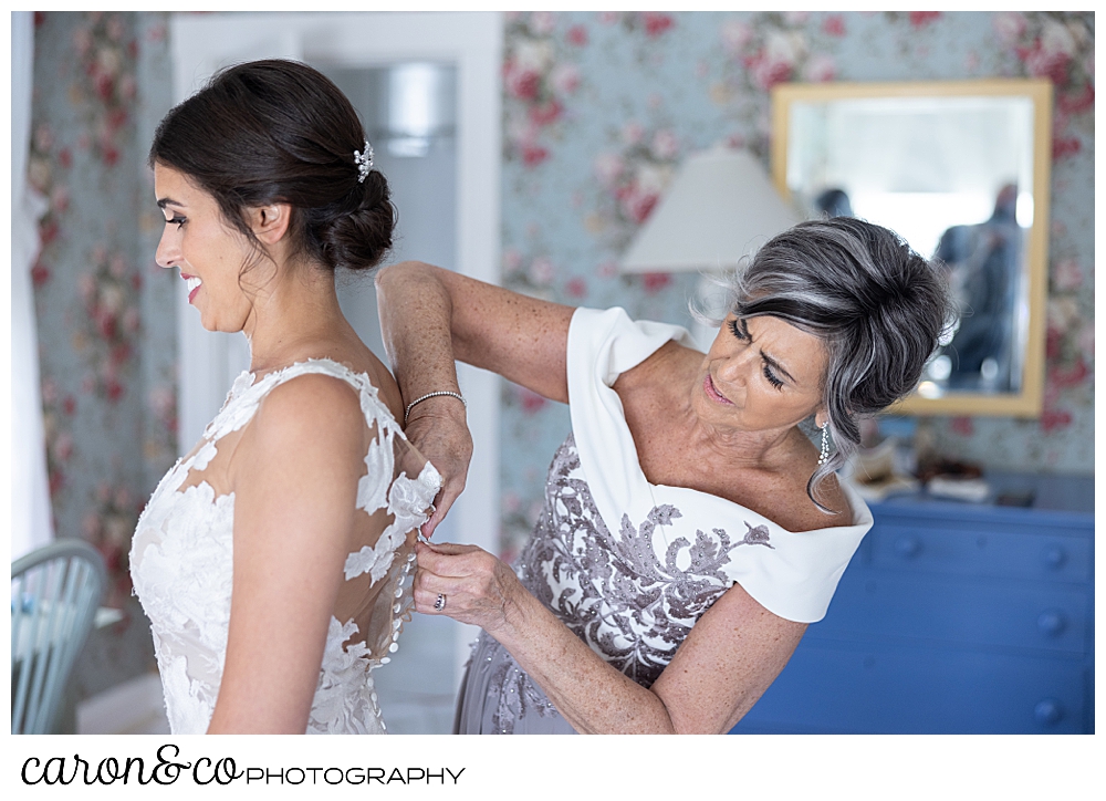 a mother helps her daughter fasten the back of her wedding dress at a coastal maine wedding at the colony hotel Kennebunkport maine