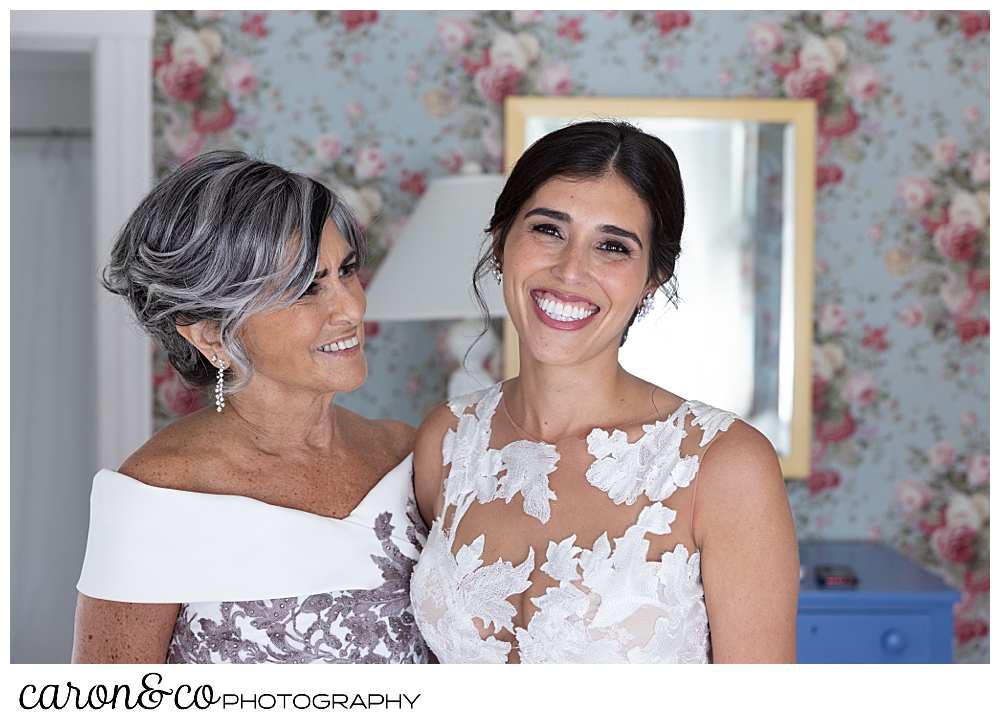 a bride and her mother stand together, the bride's mother is looking at the bride, and the bride is looking at the camera