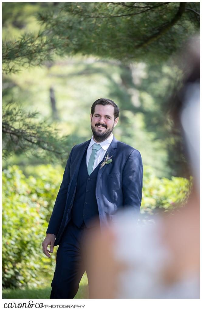 in the foreground is the shoulder and head of a dark-haired bride, in the background a groom is turning around to see her during a Maine wedding day first look at the Colony Hotel, Kennebunkport Maine