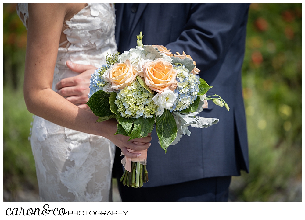 in the background is a bride and groom embracing, in the foreground is the bride's bouquet of pink, white, blue, and green