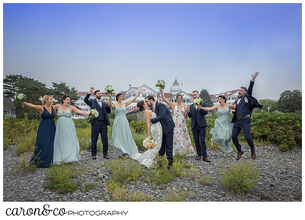 a bride and groom kiss amid their bridal party who is cheering, the colony hotel is in the background