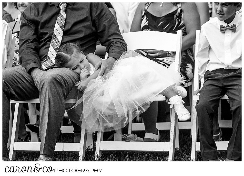 black and white photo of a flower girl resting in her chair, her head in her father's lap