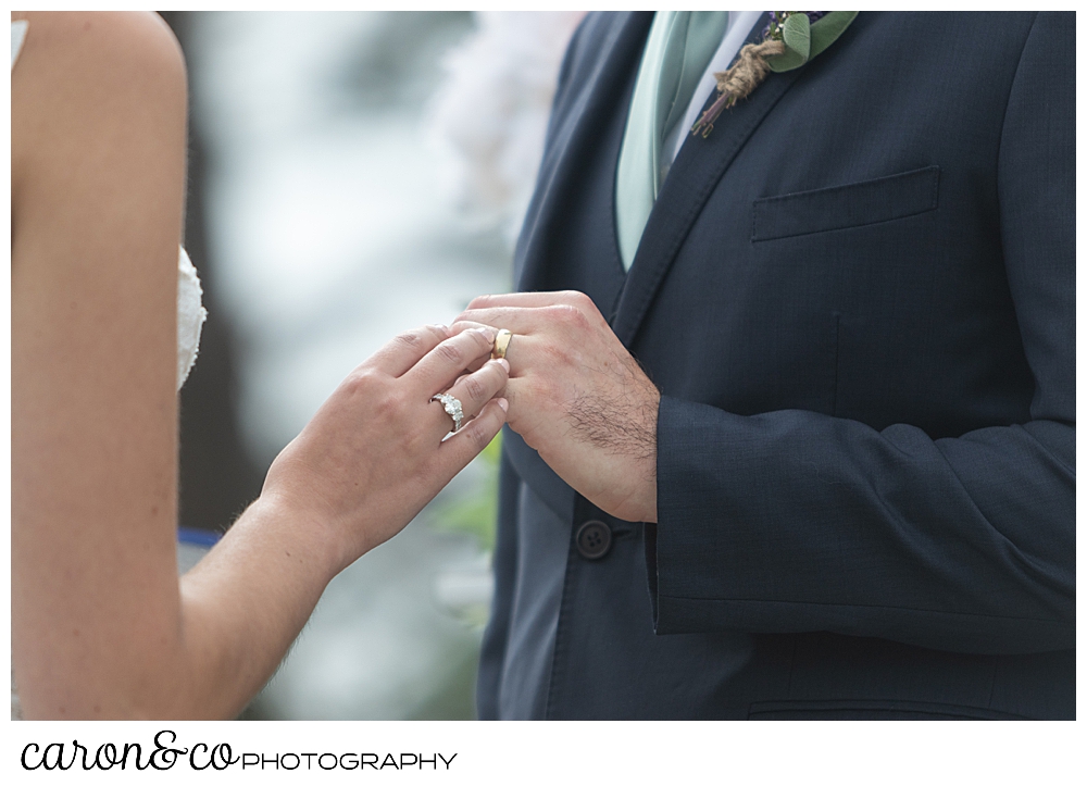 a bride's hand is putting a wedding band on a groom's hand